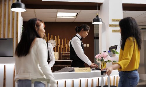 Hotel reception with two female guests Cozy hotel reception with two female guests waiting for concierge to finalize booking procedure. Relaxed customers holding baggages getting ready to check in at lavish resort